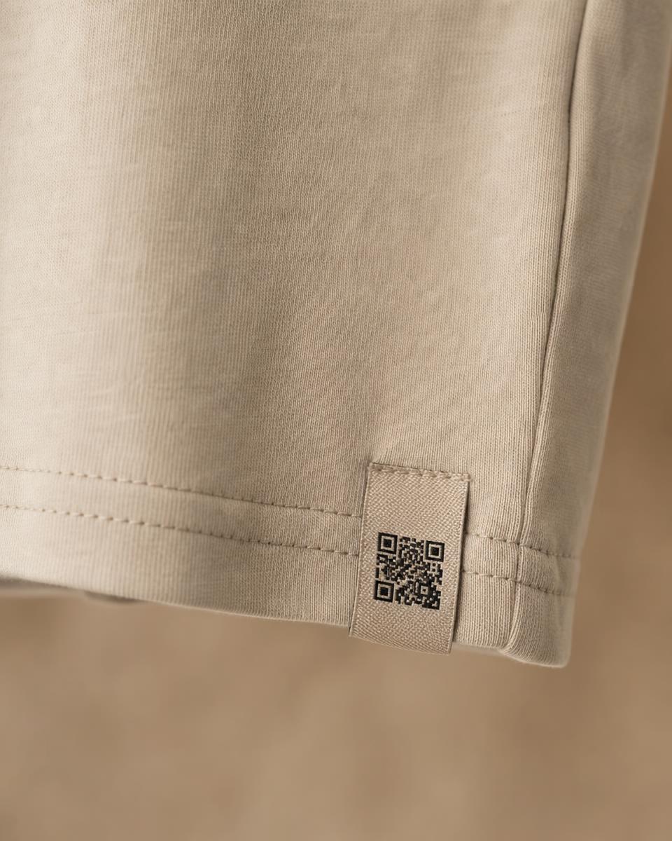 Bottom hem of a bone cotton t-shirt with a small curved woven tab carrying a square code